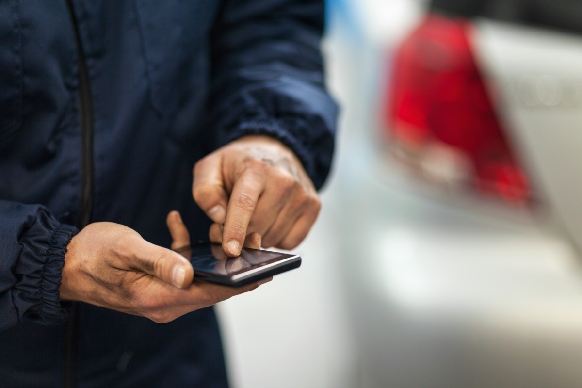 close up of a car mechanic using smart phone in repair shop