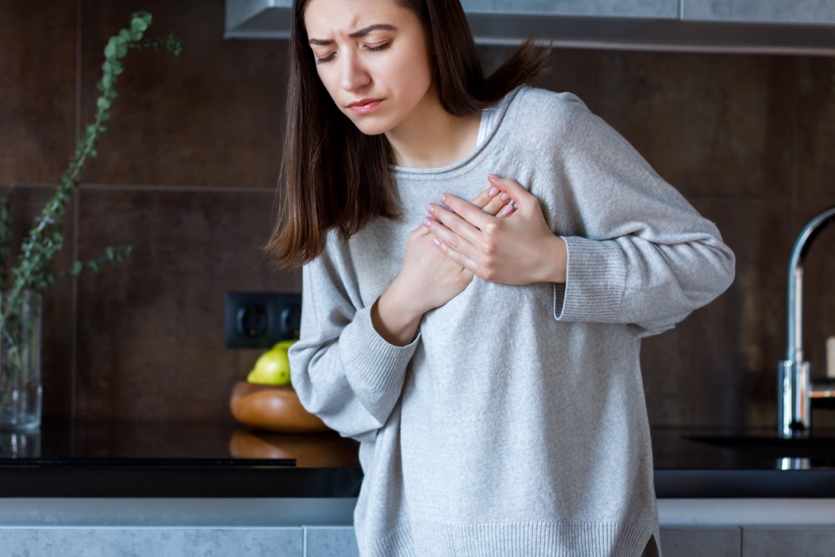 Woman in grey clothes is holding hands on her chest.