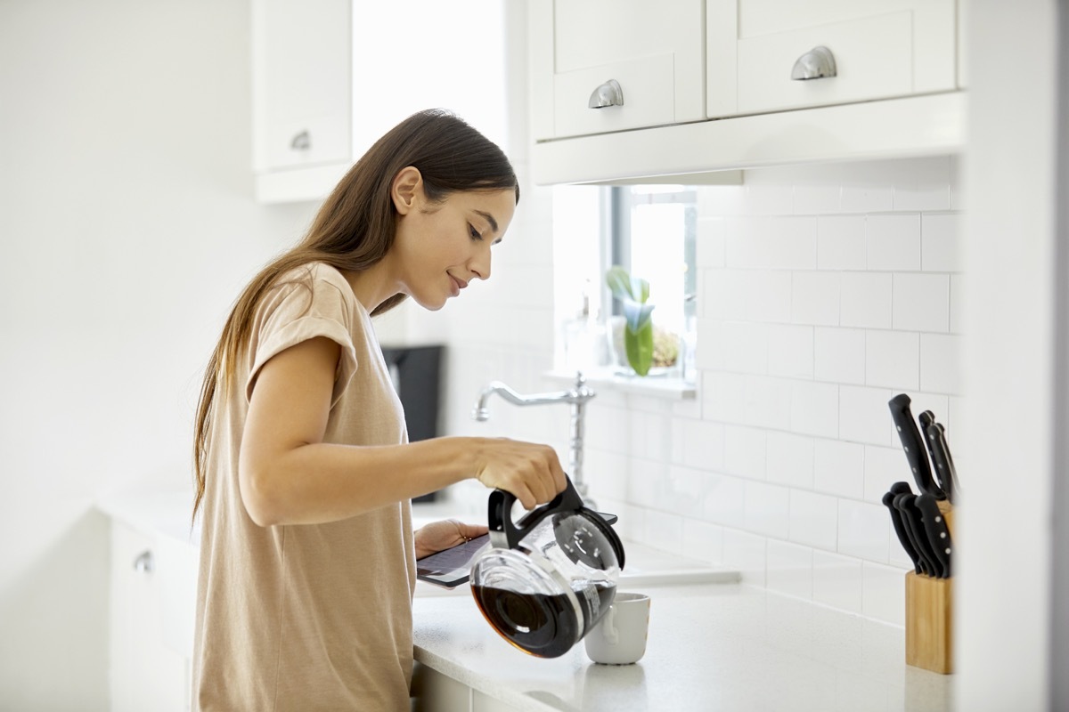 Side view of young woman pouring coffee in cup. Beautiful female is standing at kitchen counter. She is in casual at home.