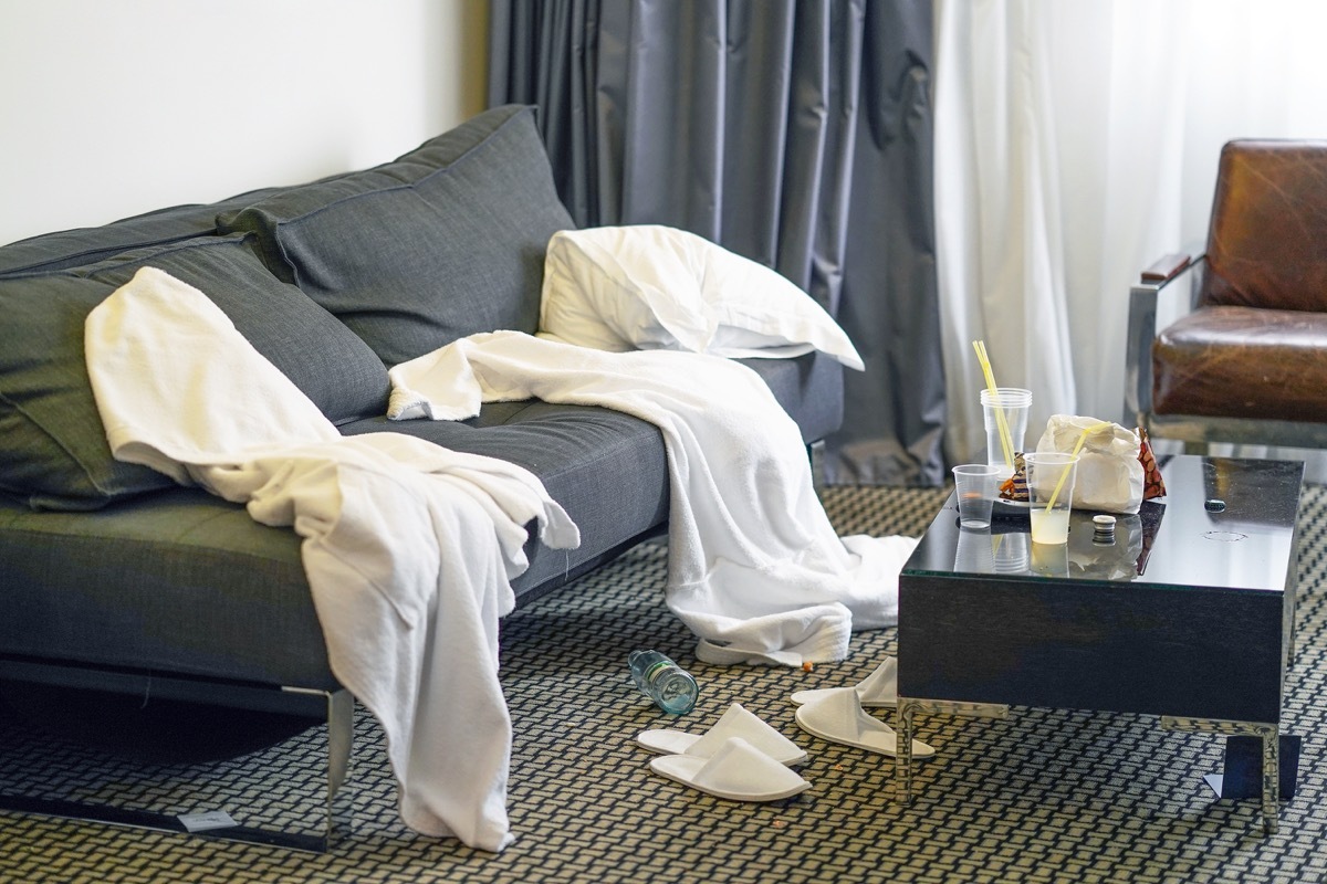 Mess in the hotel room. Scattered bathrobes and dirty and the table with the remnants of food and plastic cups.