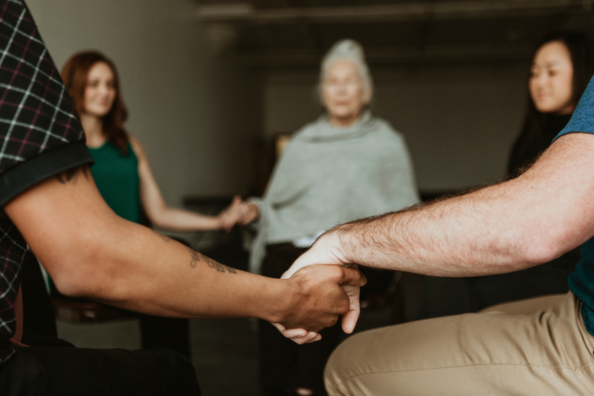 people in a recovery group, sitting in a circle and holding hands