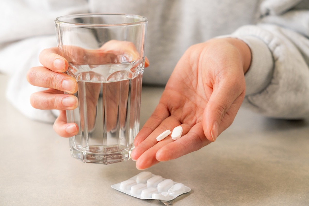 Close up showing a woman's hand, ready to take medicine with a glass of water, having taken the pills out of the blister pack.