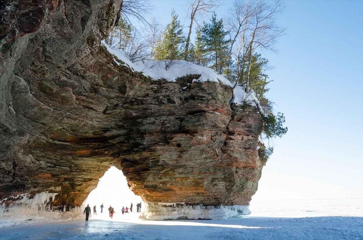 people walking underneath the rock formation on one of the apostle islands