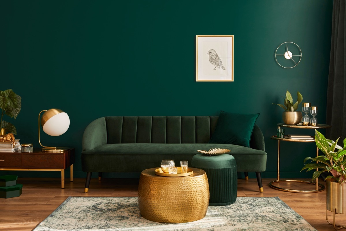 Luxury living room in house with modern interior design, green velvet sofa, coffee table, pouf, gold decoration, plant, lamp, carpet, mock up poster frame and elegant accessories. Template.