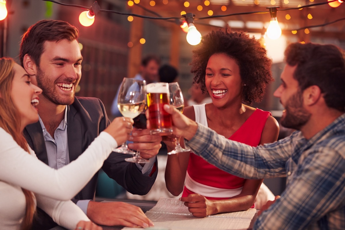 Two men and two women clinking their glasses together at a bar on a double date