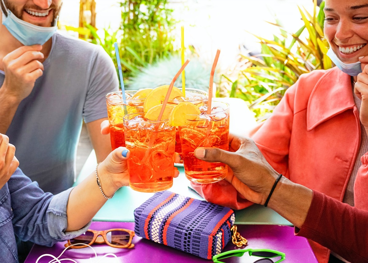 Friends drinking coktail in a restaurant bar outside in summer days with face mask on to be protected from coronavirus