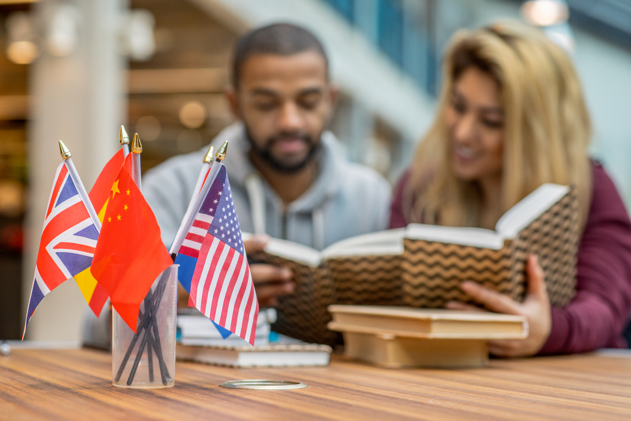 Two students sit behind a small jar of international flags while reading books and studying foreign languages