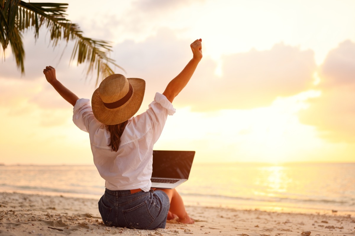 working writing funny 'out of office' messages on her laptop while sitting on the beach