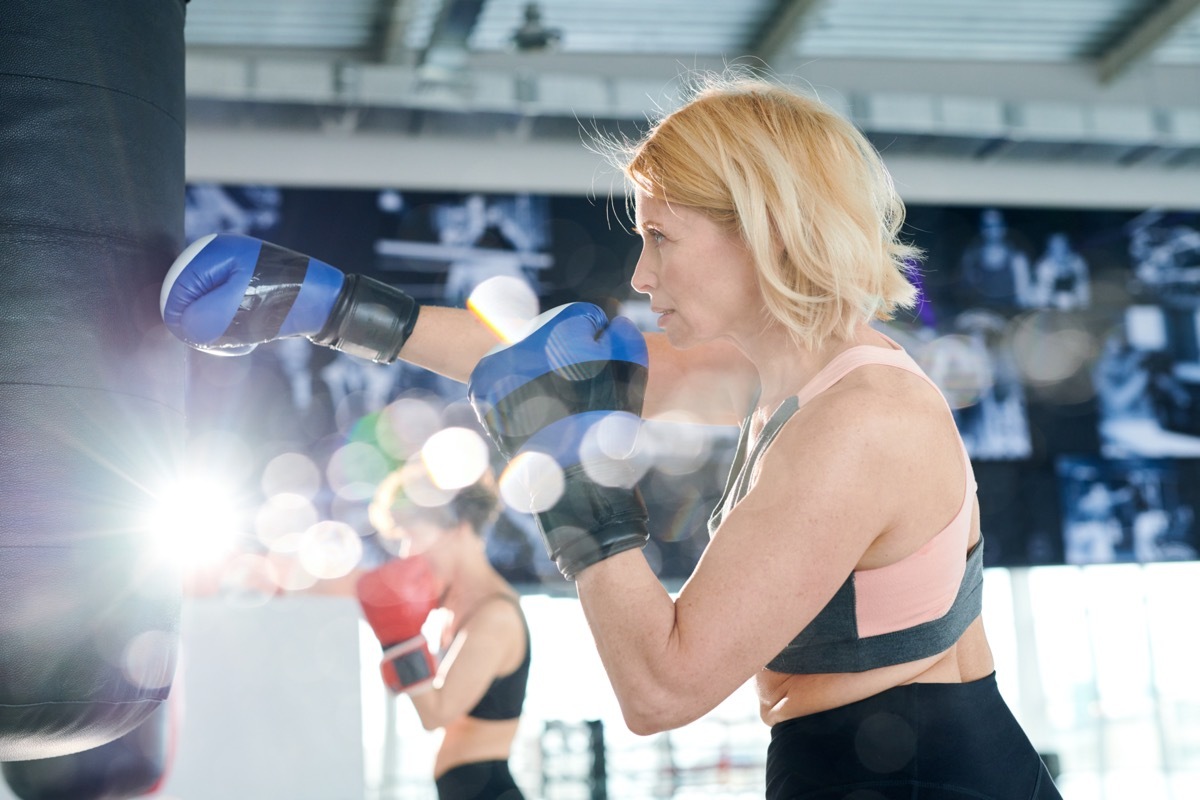 Active sportswoman in boxing gloves hitting punchbag while training in gym or contemporary leisure center