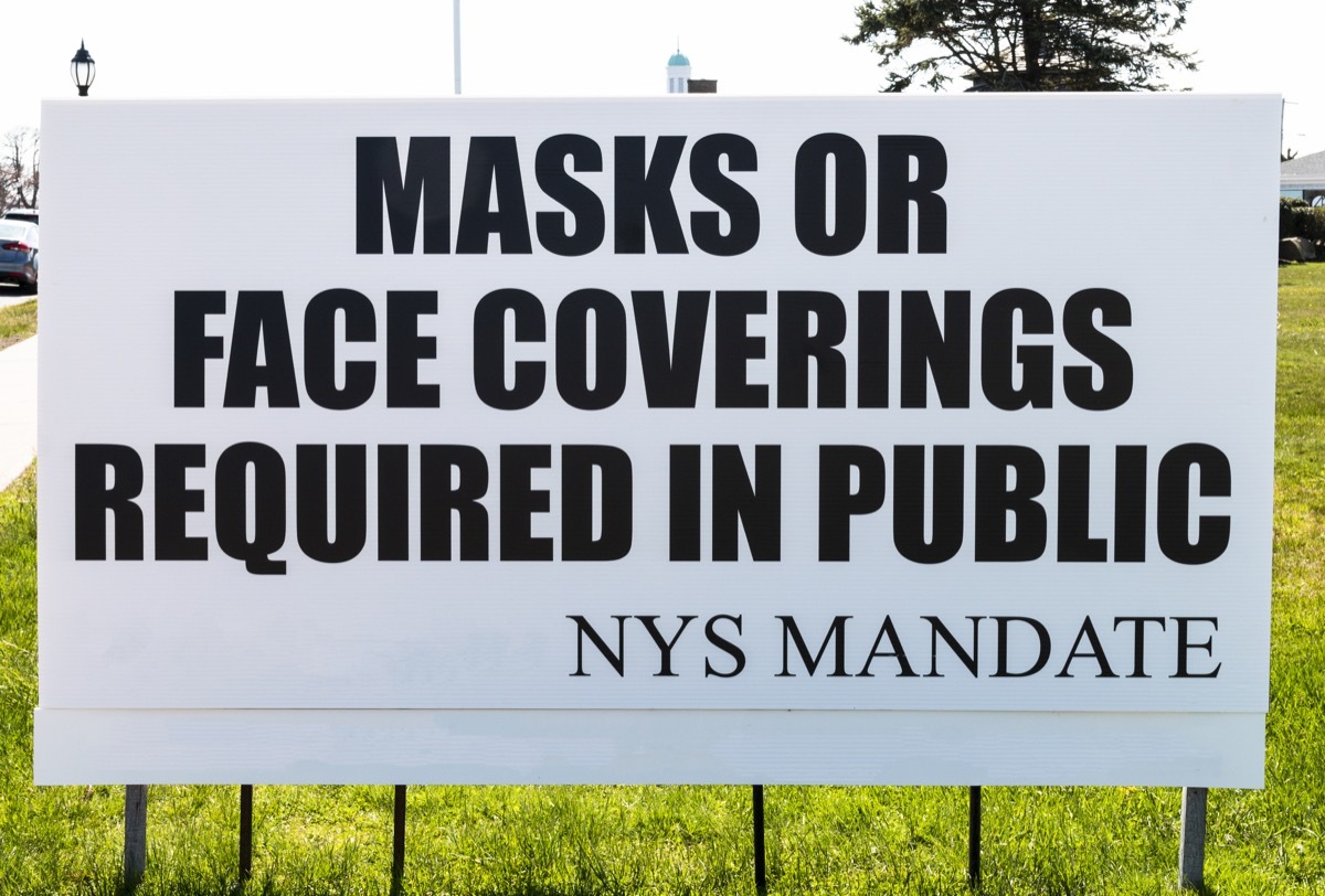 A sign on the side of the road reads Mask or Face Covering Required in Public as you enter a village in Long Island, New York.