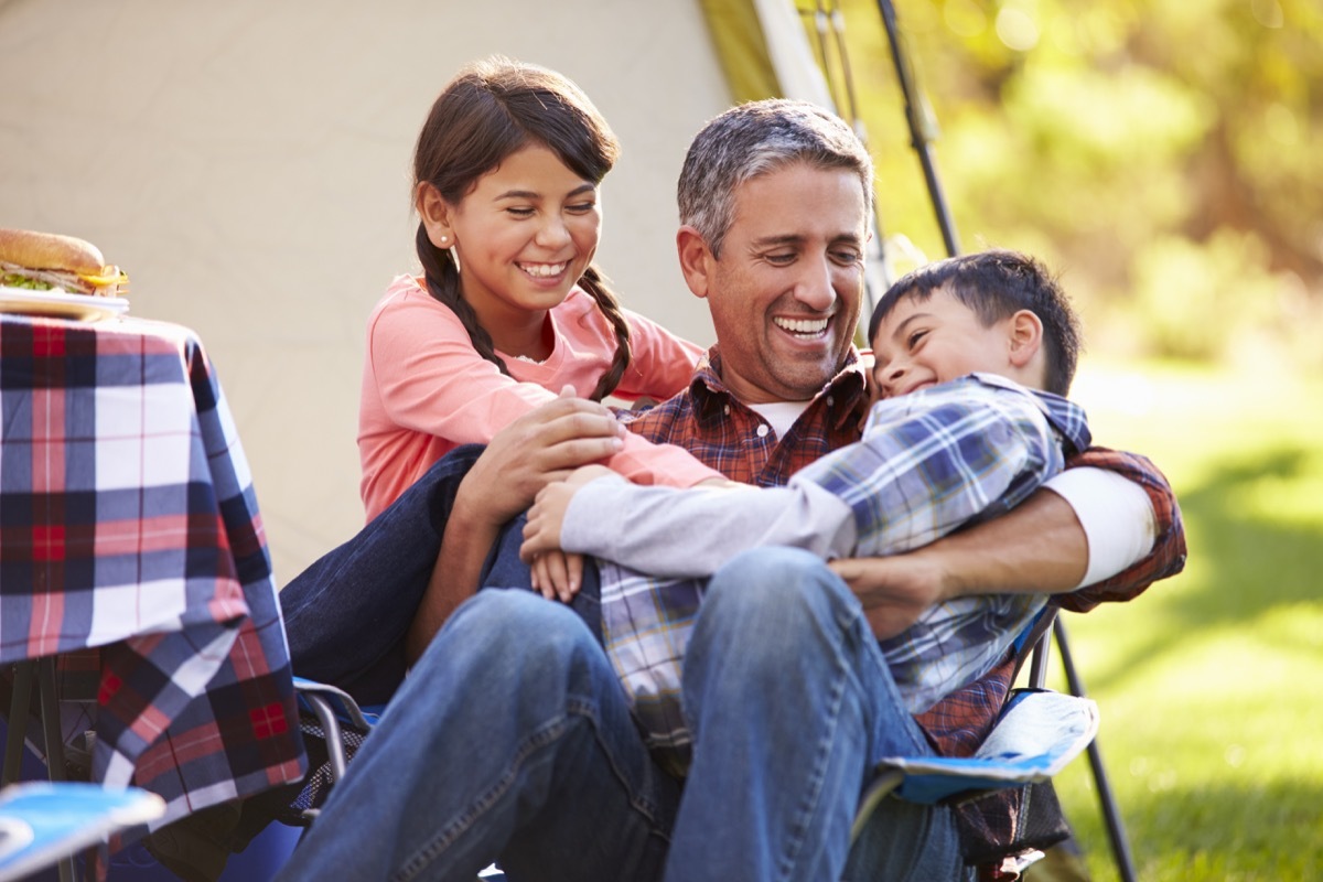 Middle aged dad laughing playing with kids while camping