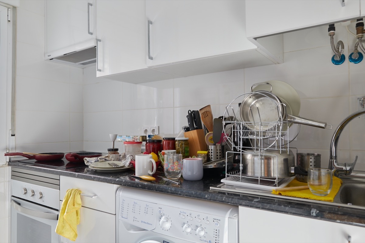 Kitchen of a house with a dirty countertop full of empty dishes and kitchen utensils for scrubbing and storage jars