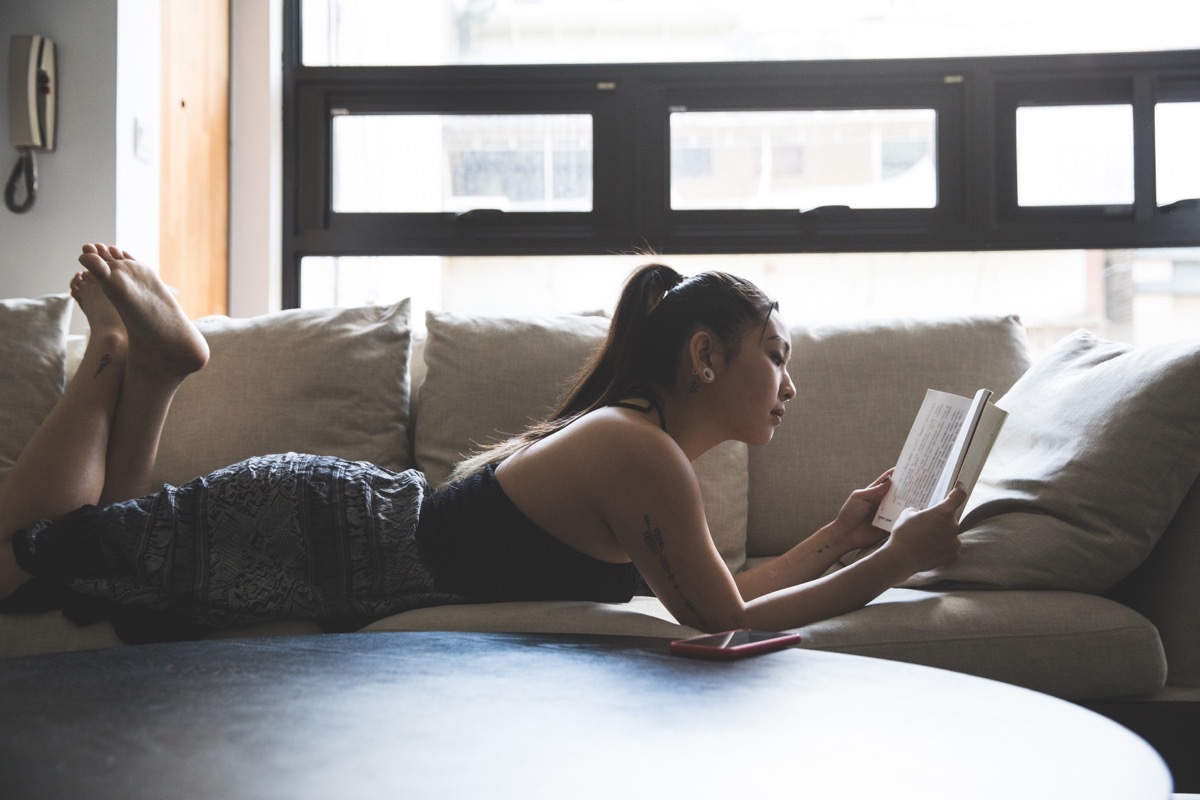 Reading a book, young woman relaxing in her living room in the morning