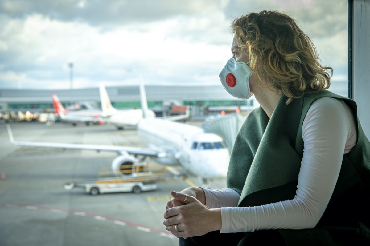 woman wearing a mask looks out the window at an airport