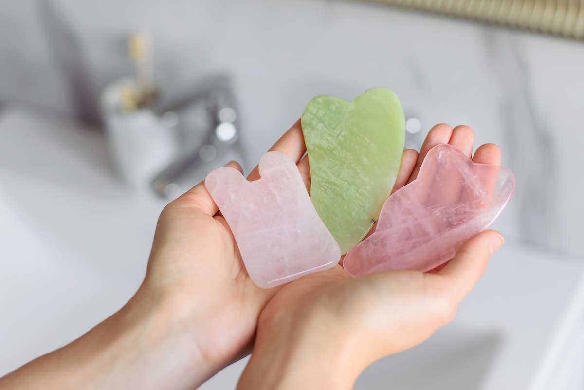 Close up of woman's. hands holding three different shaped gau sha stones in green jade and rose quartz