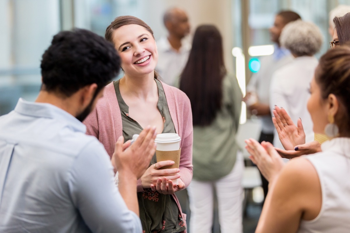 Young businesswoman has a humble expression on her face as her colleagues applaud after a presentation.