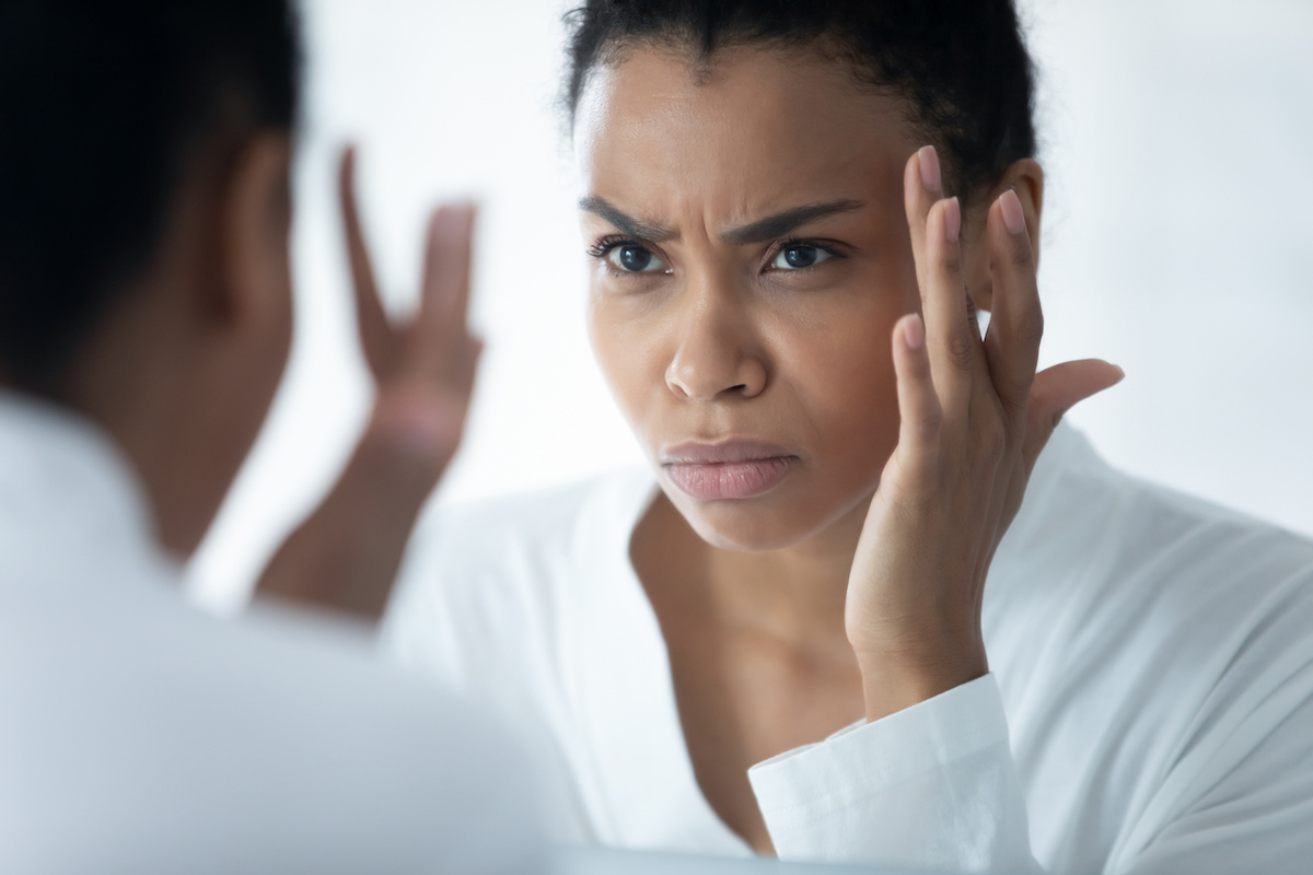 Woman wearing white bathrobe looking in mirror at eyebrow hair