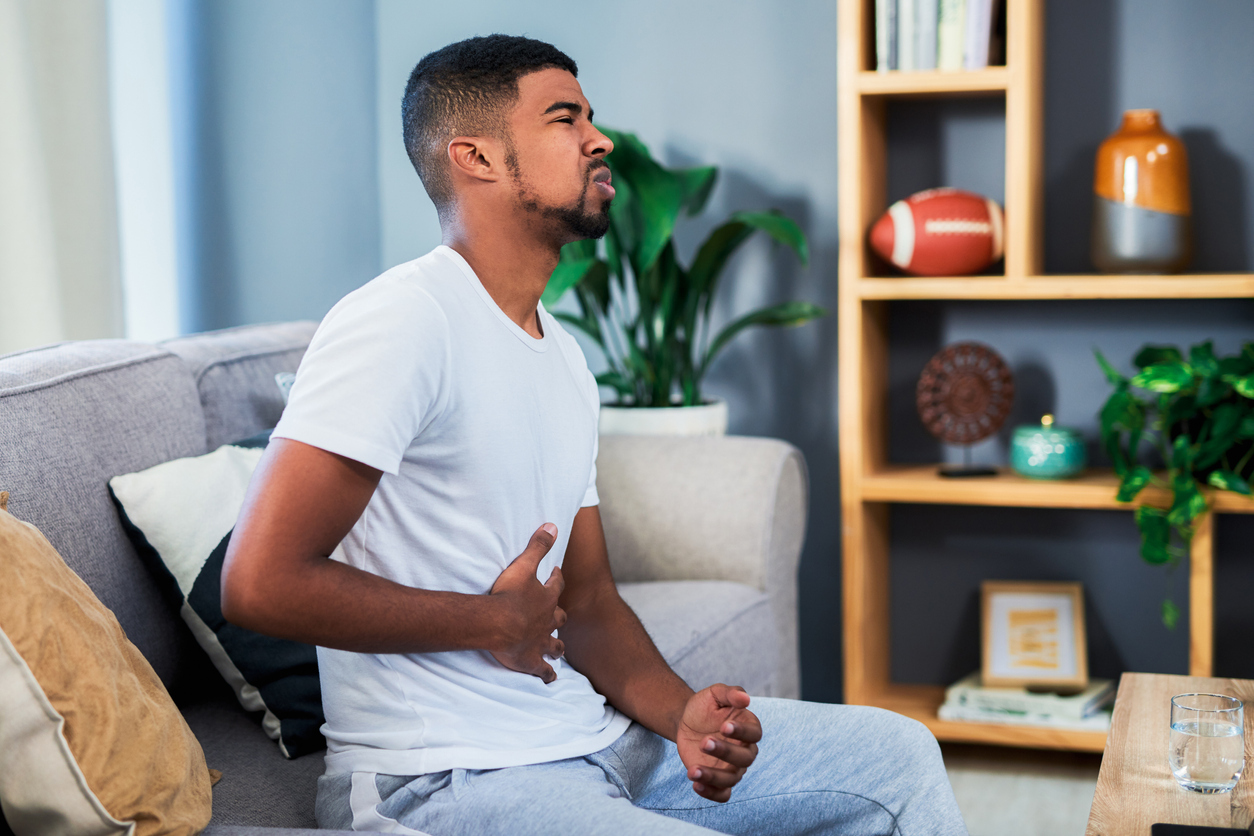 Young man sitting on couch with stomach pain.