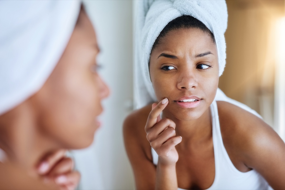 shot of a young woman inspecting her skin in front of the bathroom mirror and looking upset